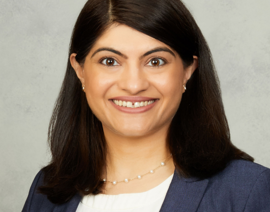 Dr. Surbhi Sidana headshot. She is smiling facing forward. She is wearing a dark blue blazer with a white blouse, as well as a necklace. She has shoulder-length dark brown hair.