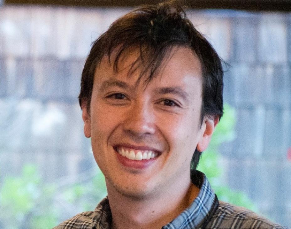 Dr. David Kurtz wearing a dark-green shirt in a brightly-lit indoor environment. He has short dark-brown hair and is smiling facing forward.