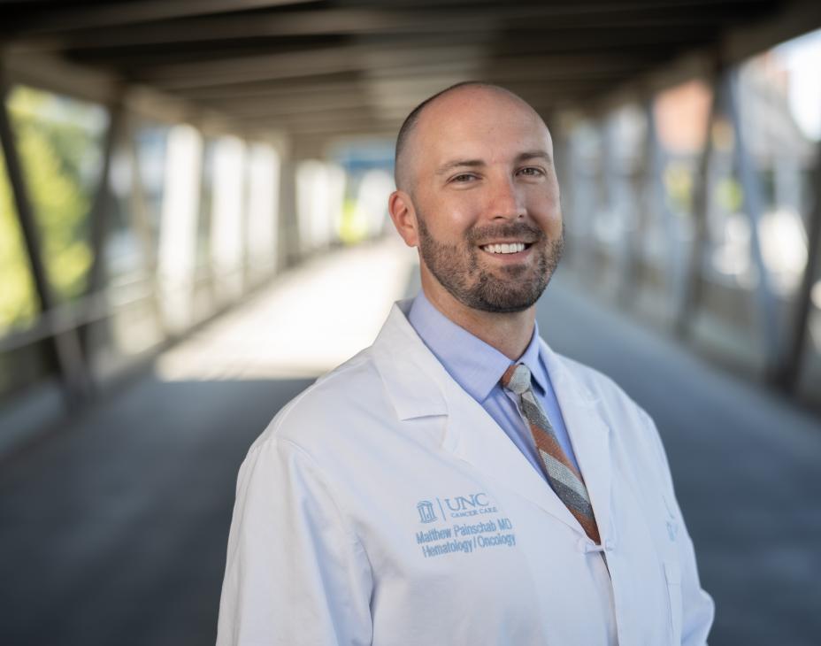 Dr. Matthew Painschab outdoors on a bridge wearing a white coat and smiling facing forward.