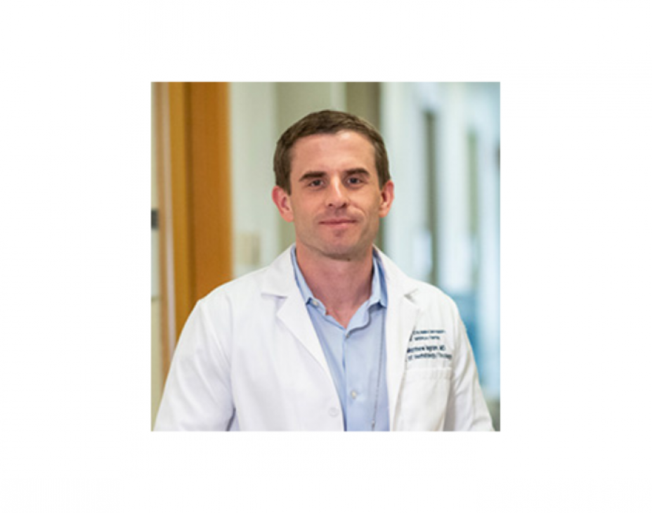 Headshot of Dr. Matthew Ingham. He is wearing a white coat and standing facing forward in a clinical setting. He is smiling and has short brown hair.