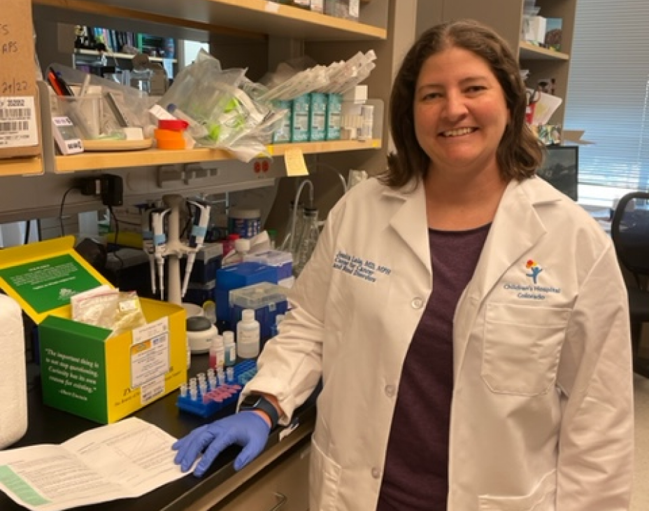 Dr. Jessica Lake in a research lab setting. She is wearing a white coat and smiling facing forward.