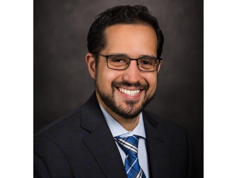 Dr. Pavlos Msaouel headshot; he is smiling facing forward against a dark-gray background.