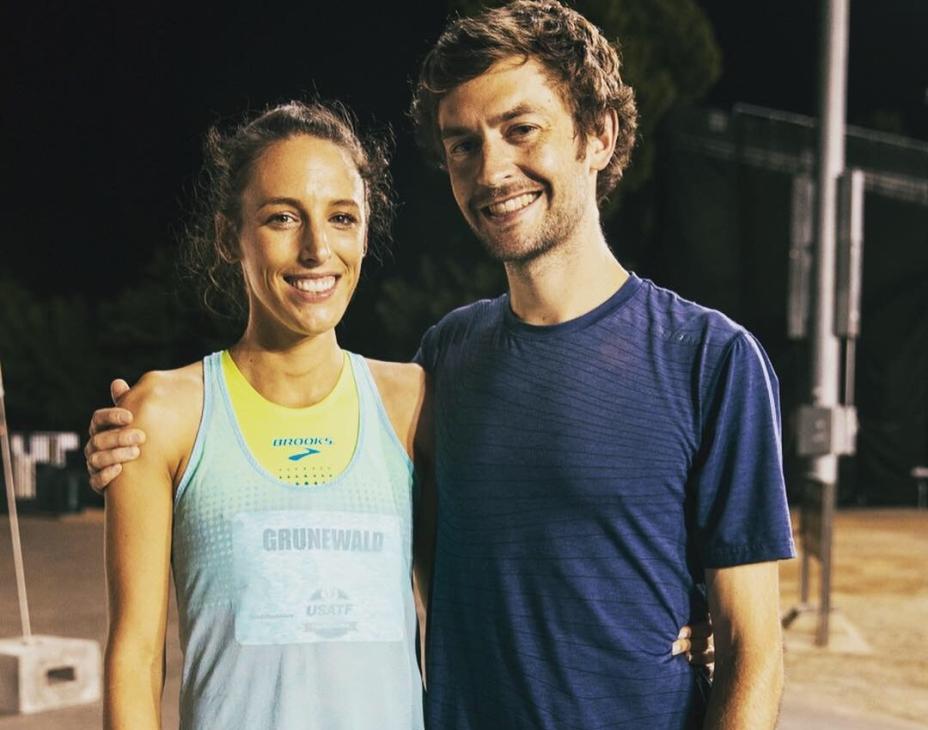 From left to right: Gabe and Justin Grunewald standing next to each other smiling, wearing athletic clothes in a track and field setting.