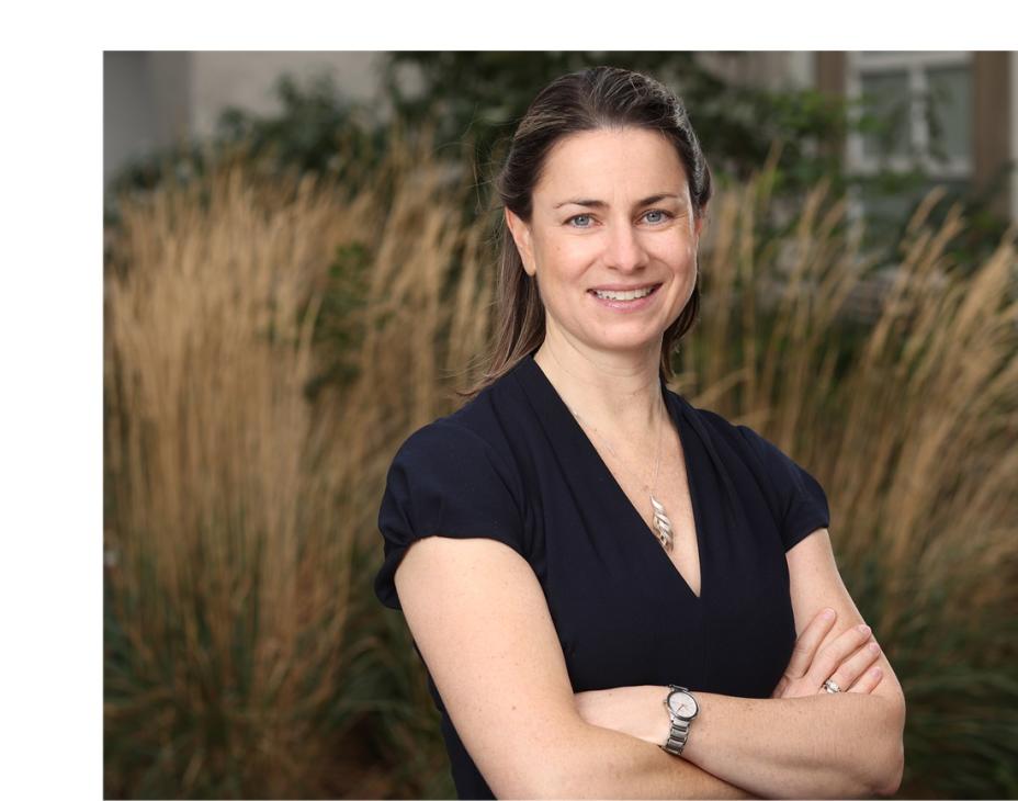 Dr. Michaela Higgins headshot. She smiling facing forward with arms crossed and is outdoors.