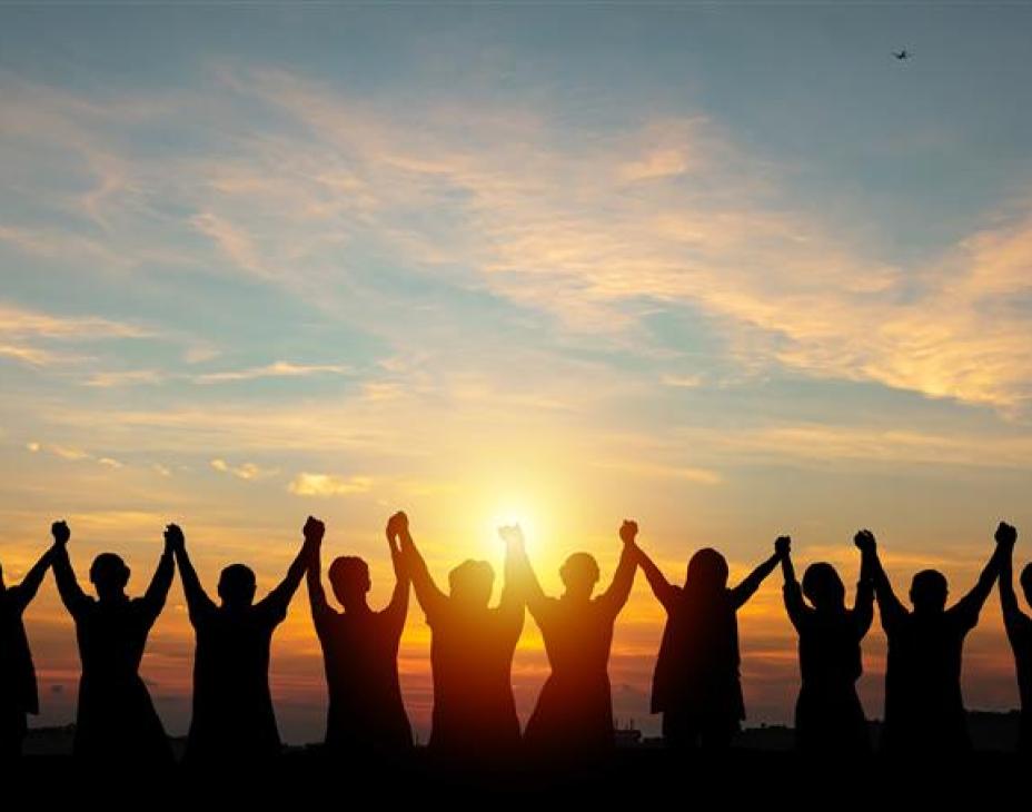 Silhouettes of people holding hands up and looking into the sunset