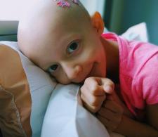 Mia headshot. She is smiling, facing forward, while laying on a sofa with one hand around her face. She is wearing a pink shirt.