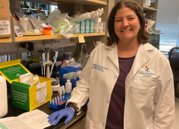 Dr. Jessica Lake in a research lab setting. She is wearing a white coat and smiling facing forward.