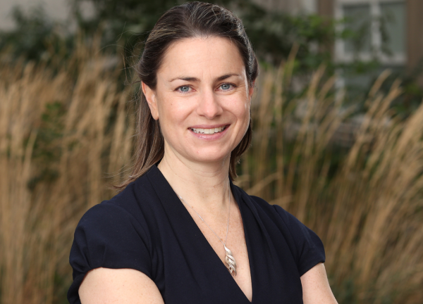 Dr. Michaela Higgins headshot. She smiling facing forward with arms crossed and is outdoors.