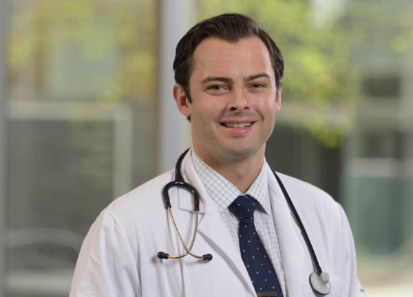 Dr. Michael Kinnaman in a doctor's coat with a stethoscope, smiling facing forward in an outdoor setting