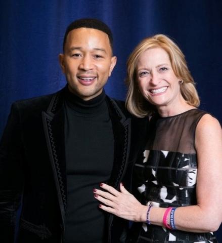 Brenda Brody smiling next to John Legend, the famous singer-songwriter. Both are wearing black clothing and smiling at the camera.
