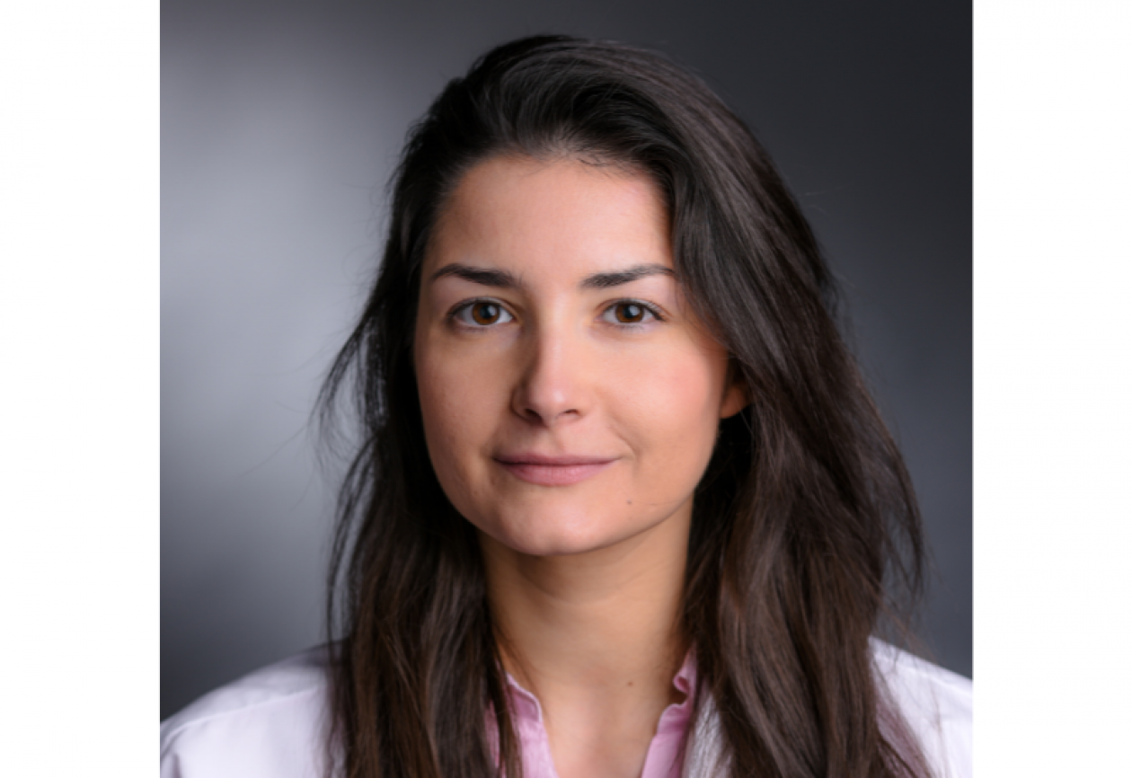 Dr. Ana Garrido-Castro headshot. She is smiling facing forward against a dark gray background, with shoulder-length brown hair.