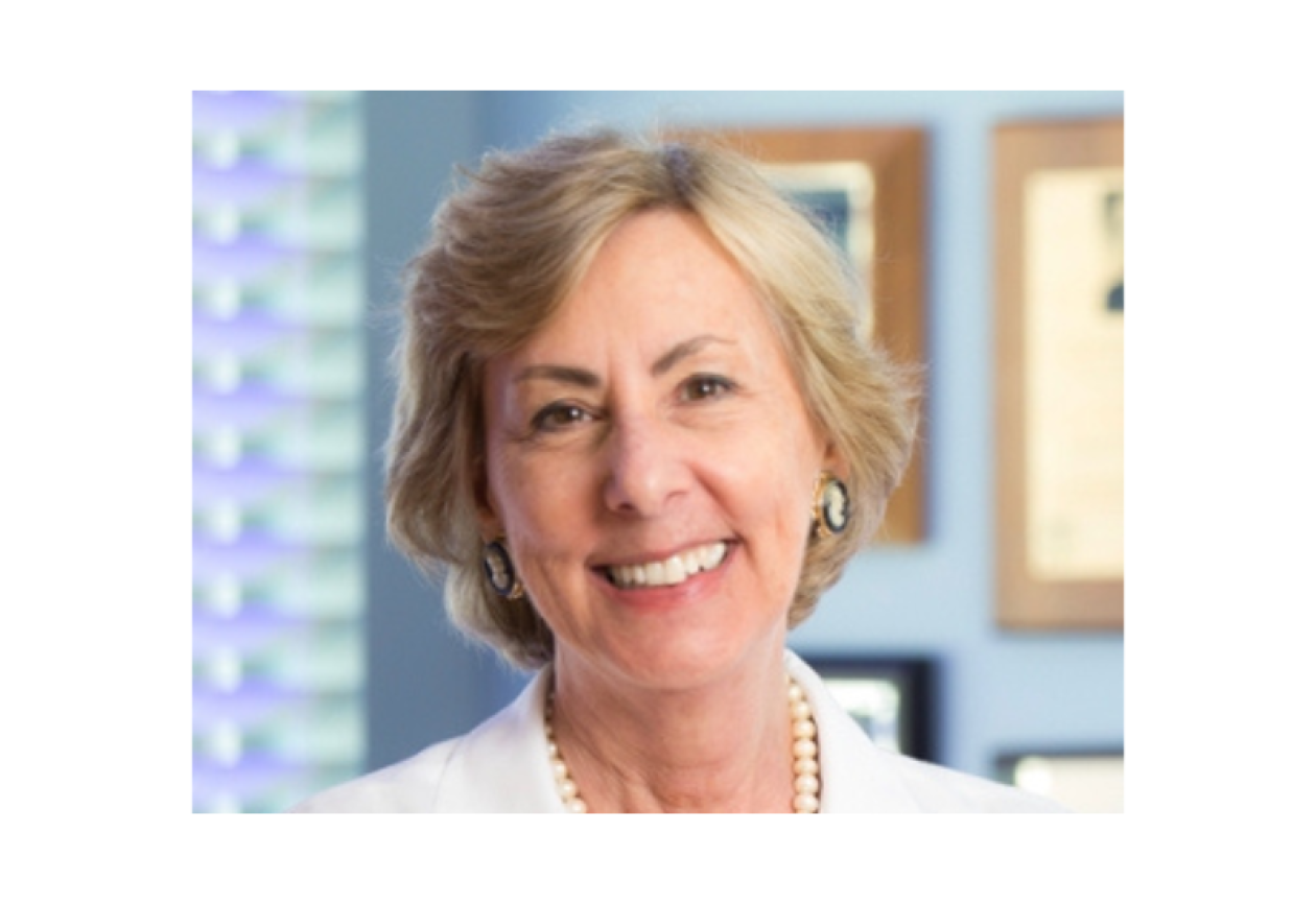 Dr. Carolyn Runowicz smiling facing forward in a clinical setting. She is wearing a white coat and pearl necklace.