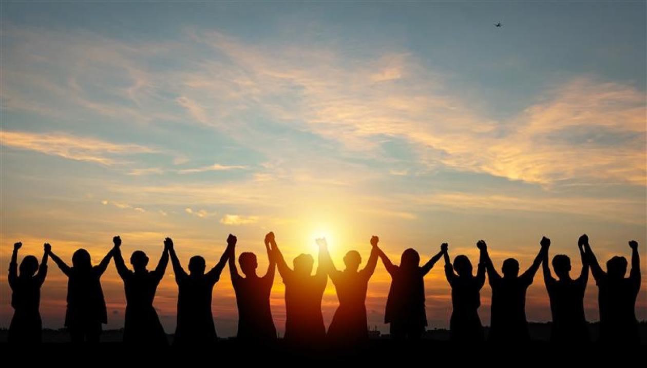 Silhouettes of people holding hands up and looking into the sunset