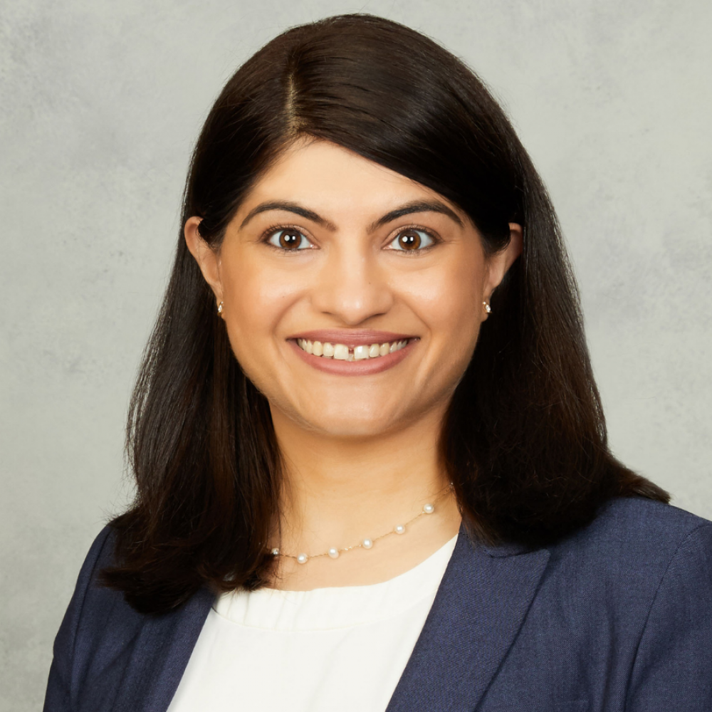 Dr. Surbhi Sidana headshot. She is smiling facing forward. She is wearing a dark blue blazer with a white blouse, as well as a necklace. She has shoulder-length dark brown hair.