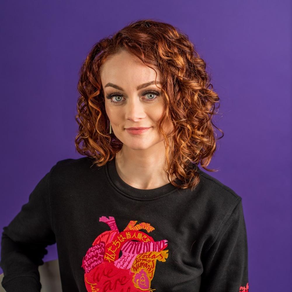 Kristin Flanary headshot. She has shoulder-length auburn red hair and is smiling facing forward against purple background.