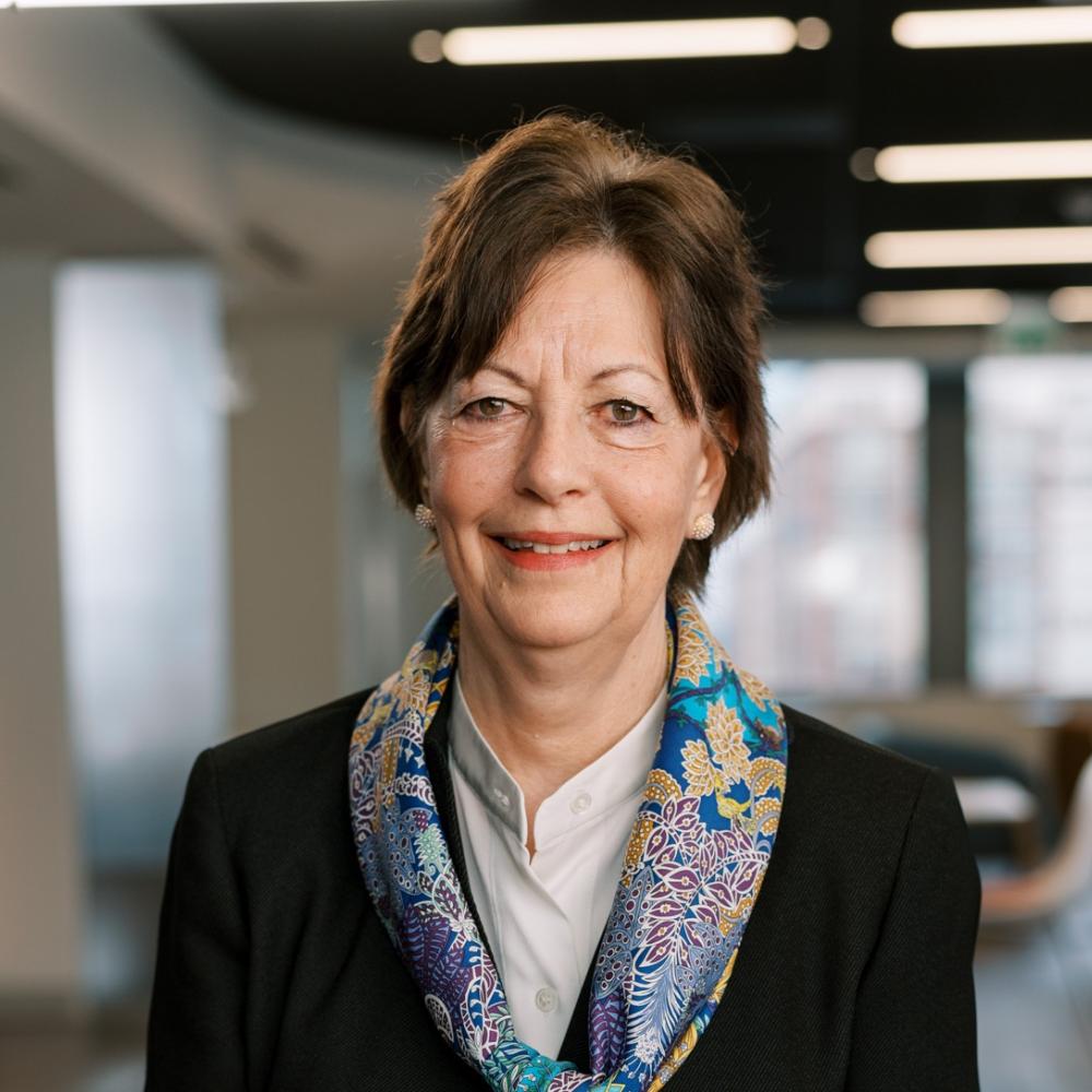 Headshot of Dr. Lynn Schuchter. She has short dark-brown hair and is wearing a black jacket with a turquoise floral scarf.