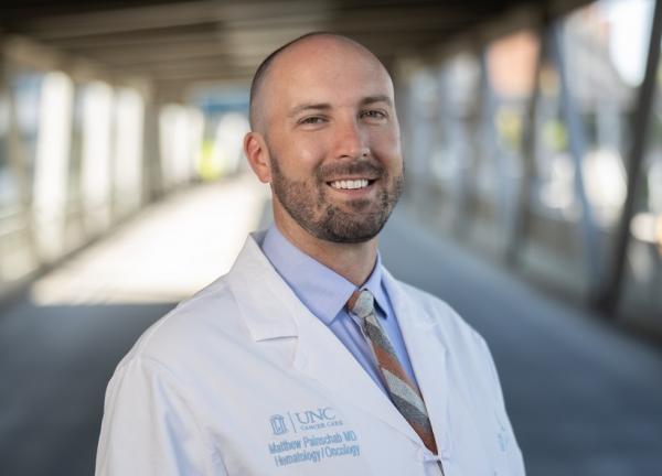 Dr. Matthew Painschab outdoors on a bridge wearing a white coat and smiling facing forward.